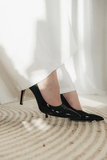 Schwarze Pumps auf einem geflochtenen Teppich vor einem hellen Vorhang