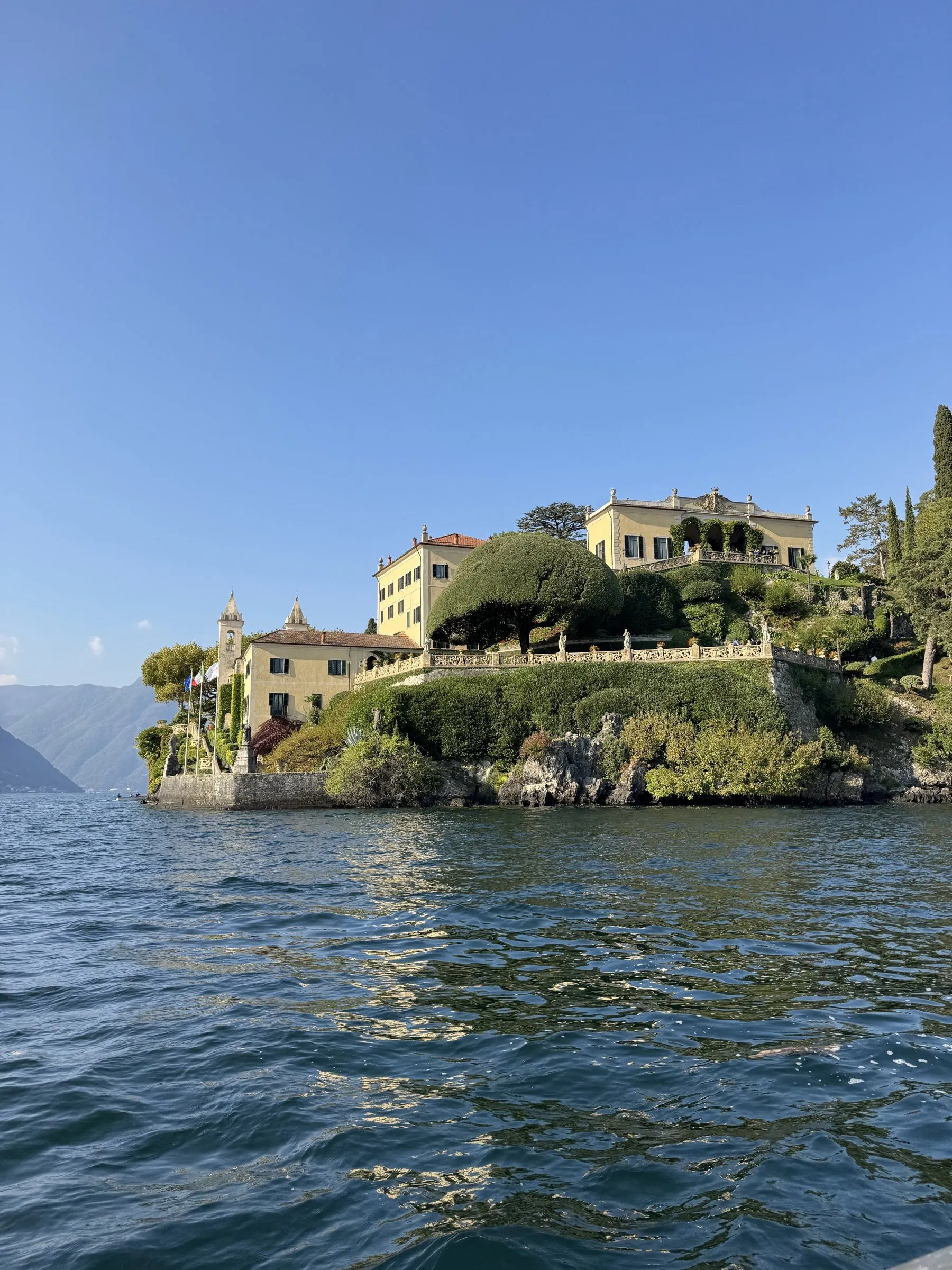 Gelbe Villa mit Gärten auf einer Landzunge am See, davor das blaue Wasser